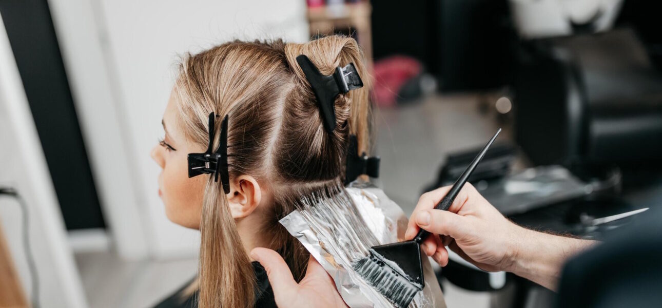 Hairdresser is applying bleaching powder on woman's hair and wrapping into the foil.